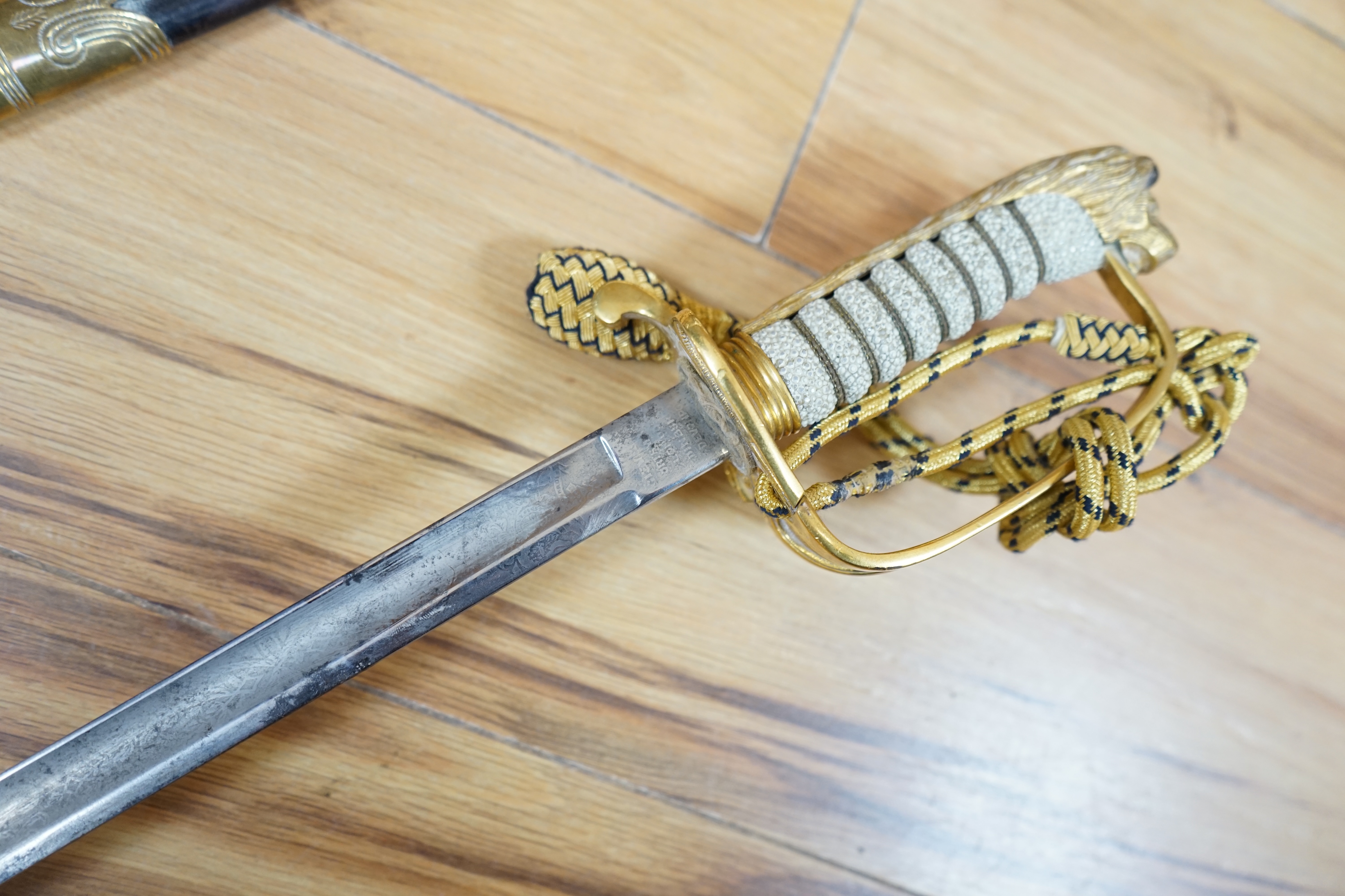 A Victorian Royal Navy officer’s sword by Grieves, engraved blade, lion’s head pommel, fish skin grip, folding guard engraved with R.J. Murray, with its sword knot and leather scabbard with brass mounts, blade 79cm. Cond